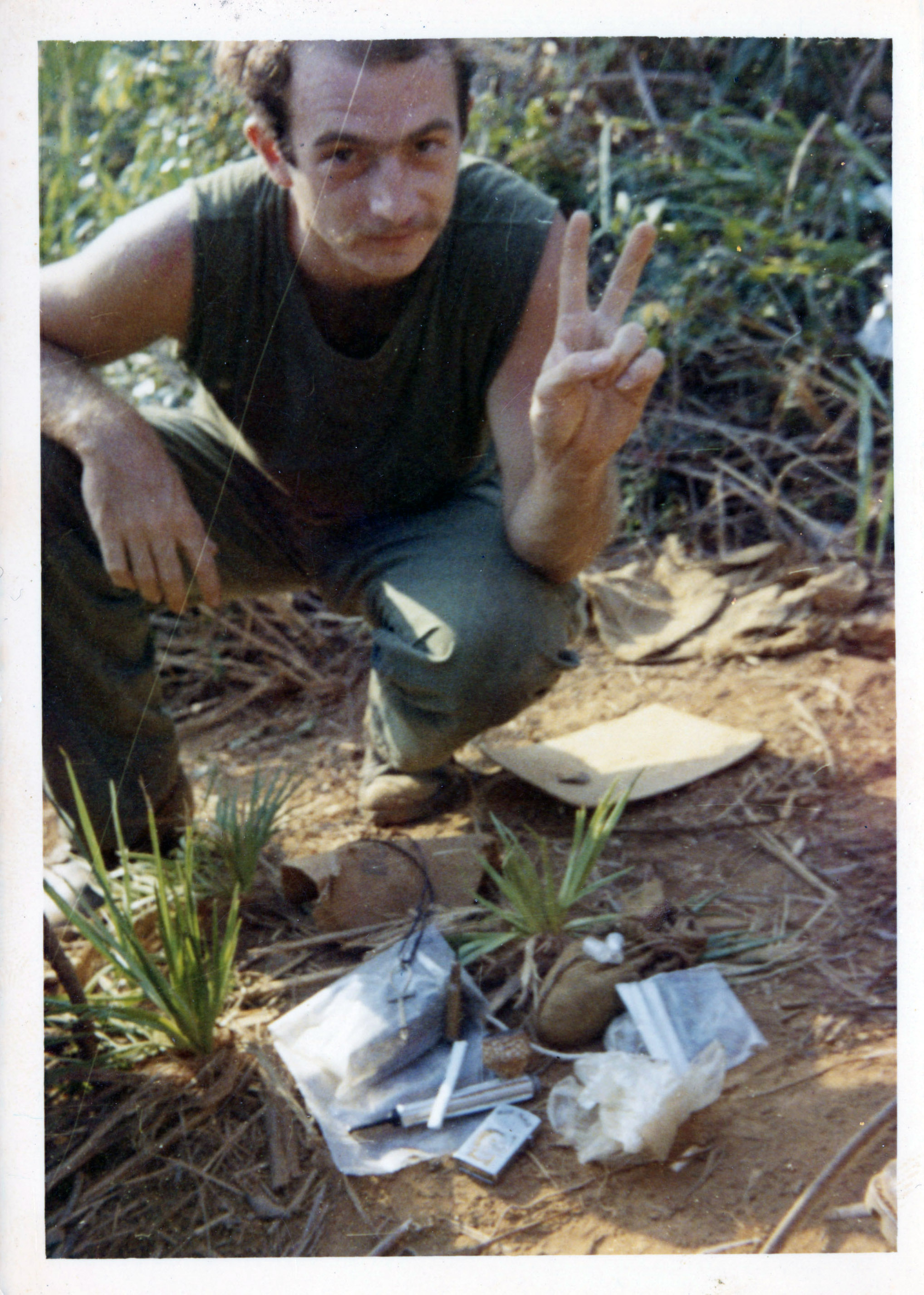 A soldier poses with plastic bags and rolled joints while holding up the peace symbol with his hand.