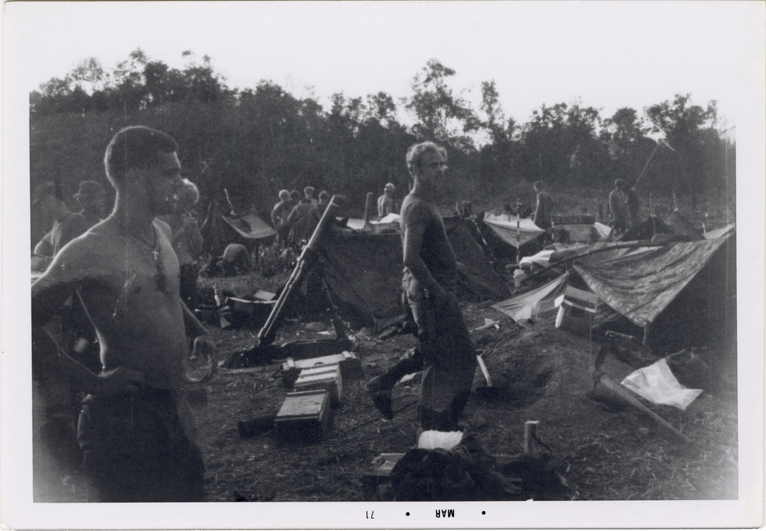 Two soldiers are standing in the base camp, staring in the same direction off to the right.