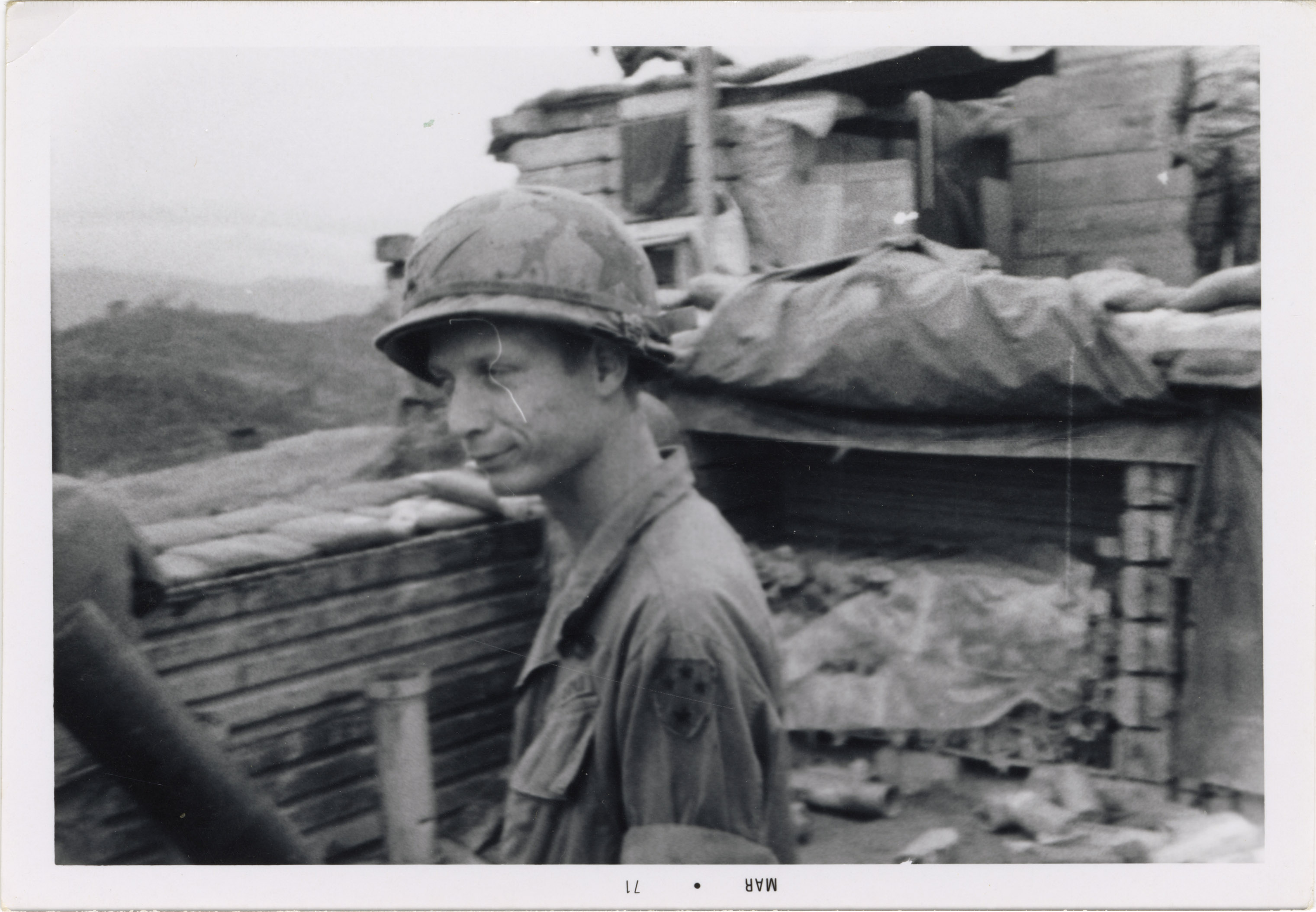 A soldier in the Vietnam war is looking out while standing in a dugout at base camp.