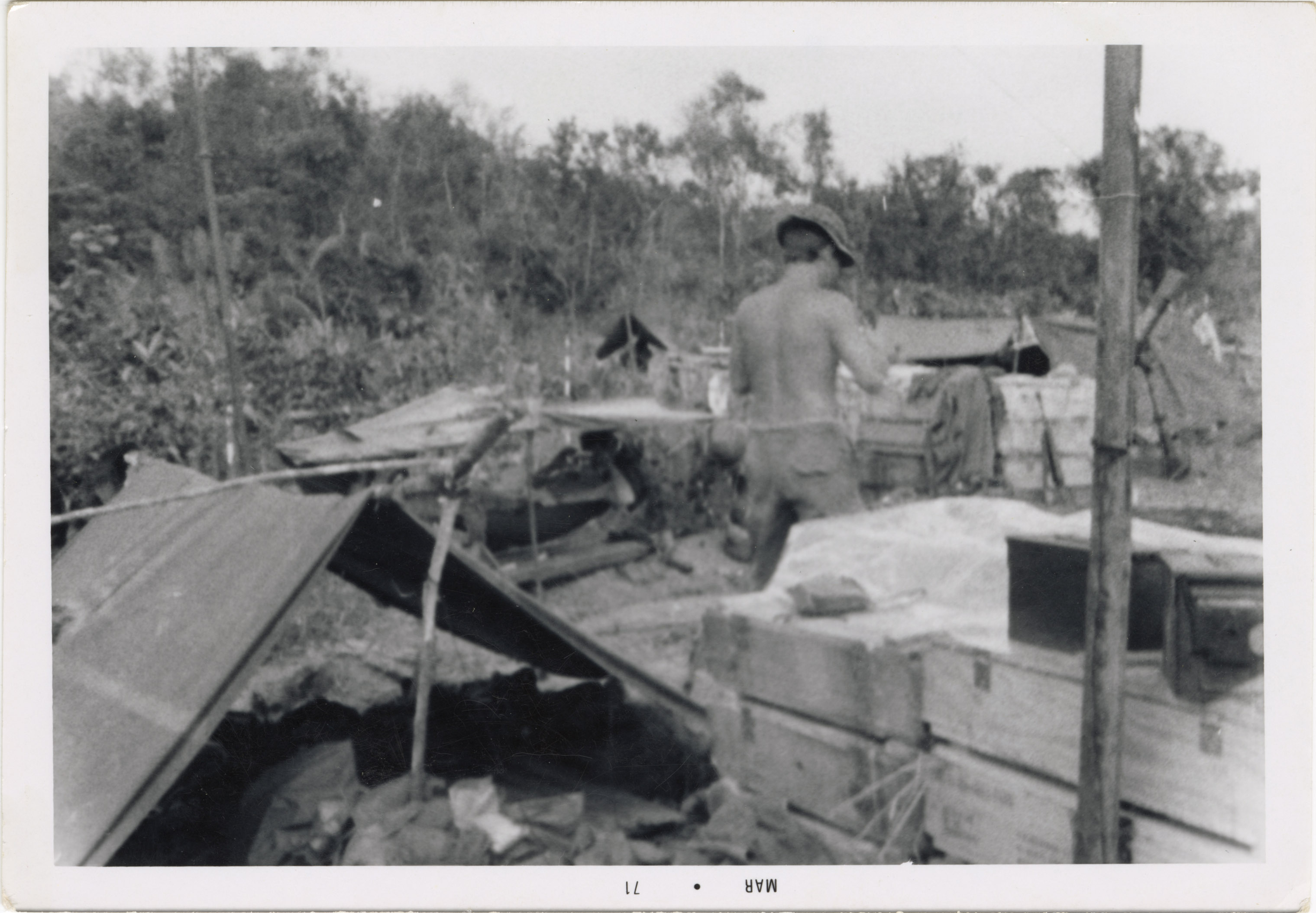 A soldier stands near a tent in the base camp, appearing to be working on something out of view.