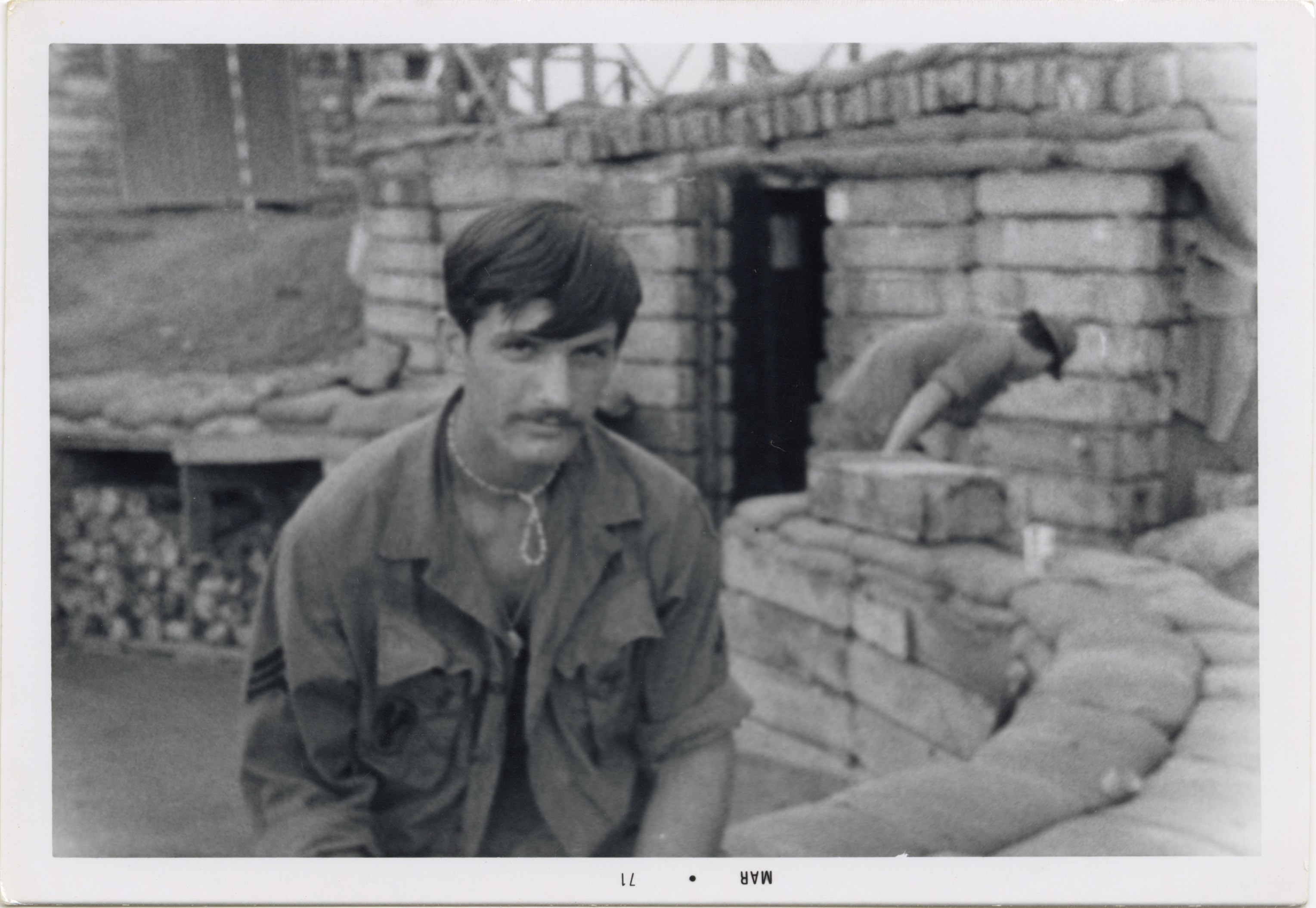 Soldier poses for camera while looking somber and istting on a brick wall at the base camp.